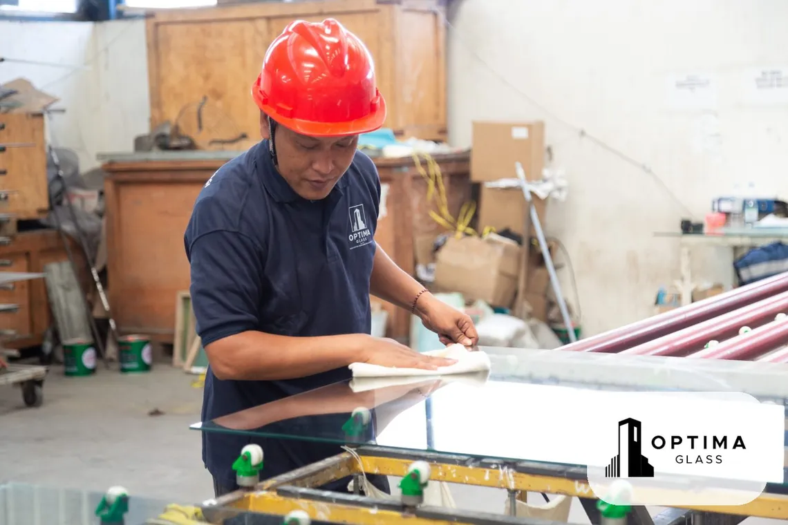 Pekerja Optima Glass membersihkan kaca sebelum diproses
