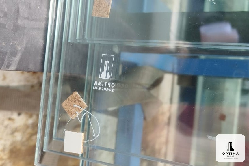 Kaca tempered Optima Glass dengan logo Optima Tempered Glass di sudut kaca