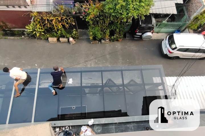 Tukang kaca memasang lembar kaca kanopi di atas rangka