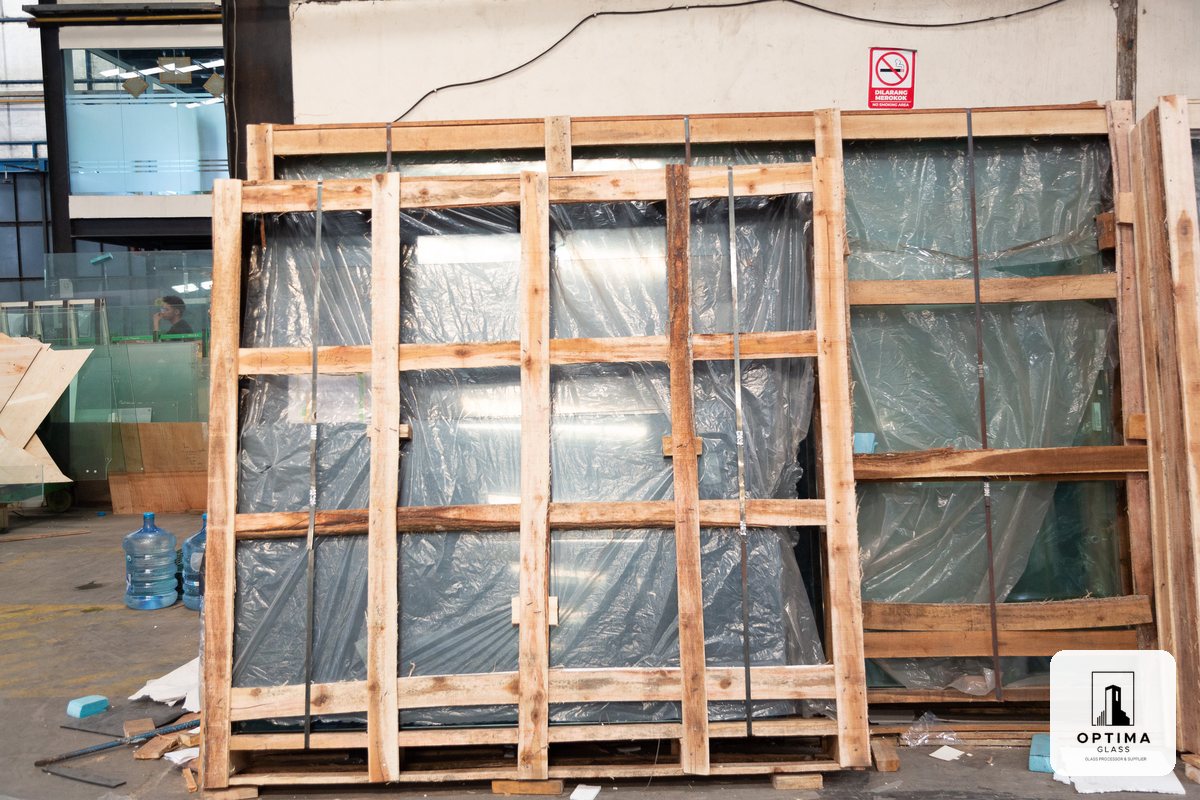 Kaca tempered dikemas dalam rak kayu di gudang pabrik Optima Glass