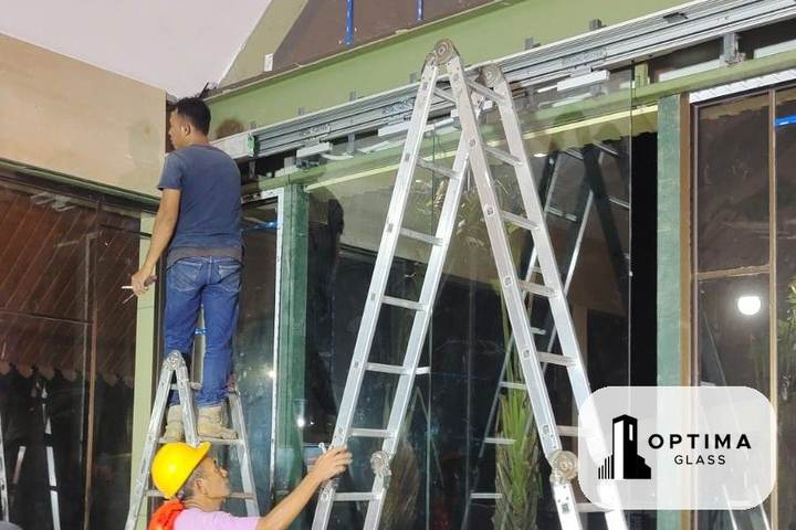 Pemasangan pintu kaca frameless dan fitting di bagian atas pada malam hari