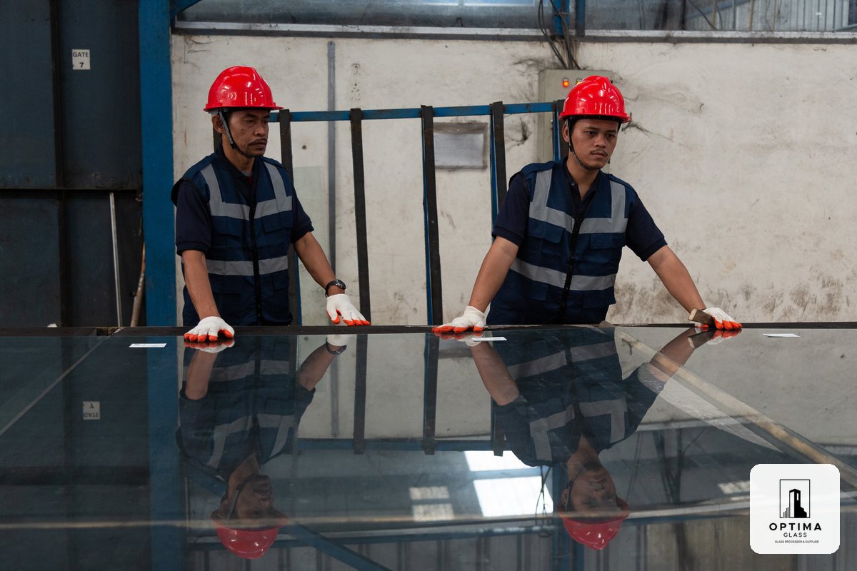 Dua operator Optima Glass menangani satu lembar kaca di pabrik Cikarang
